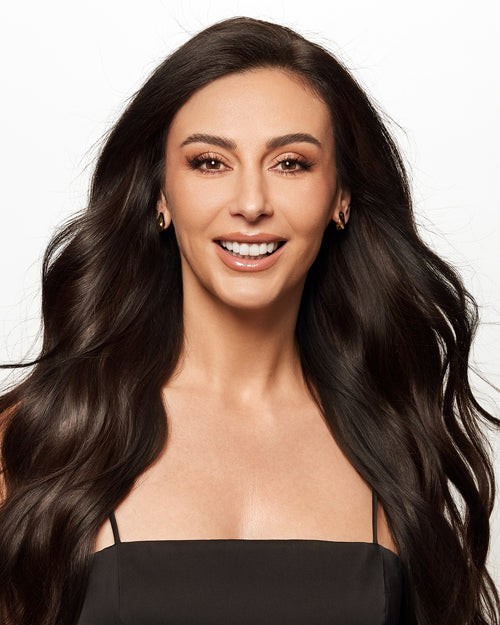 Portrait of a smiling woman with voluminous, long dark wavy hair parted down the middle.