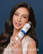 Smiling woman with long, wavy dark hair holding a bottle of anti-dandruff shampoo.