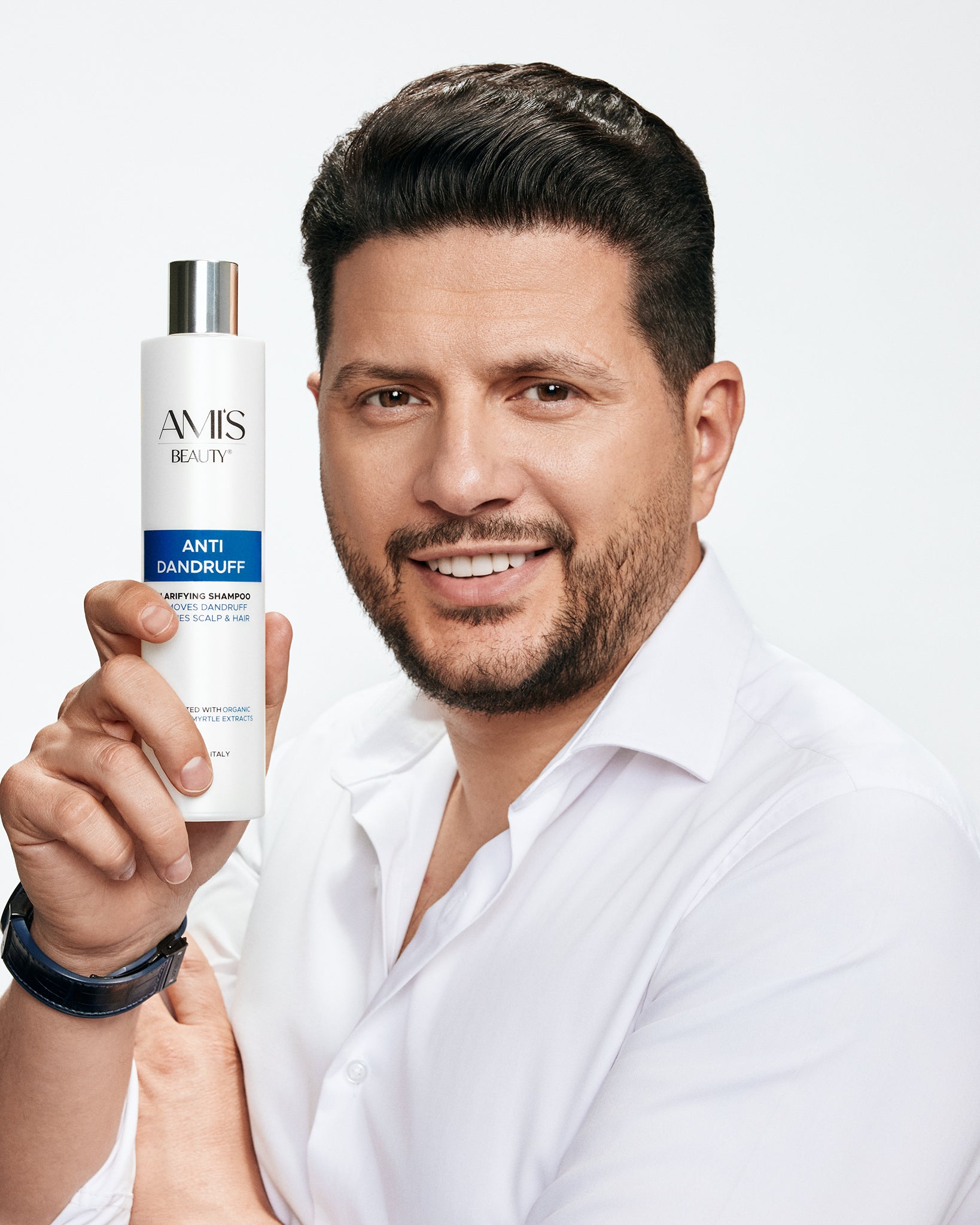 Smiling man in a white shirt holding a bottle of anti-dandruff shampoo next to his face.