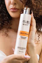 Woman with dark curly hair holding a bottle of Curly Crush Shampoo.