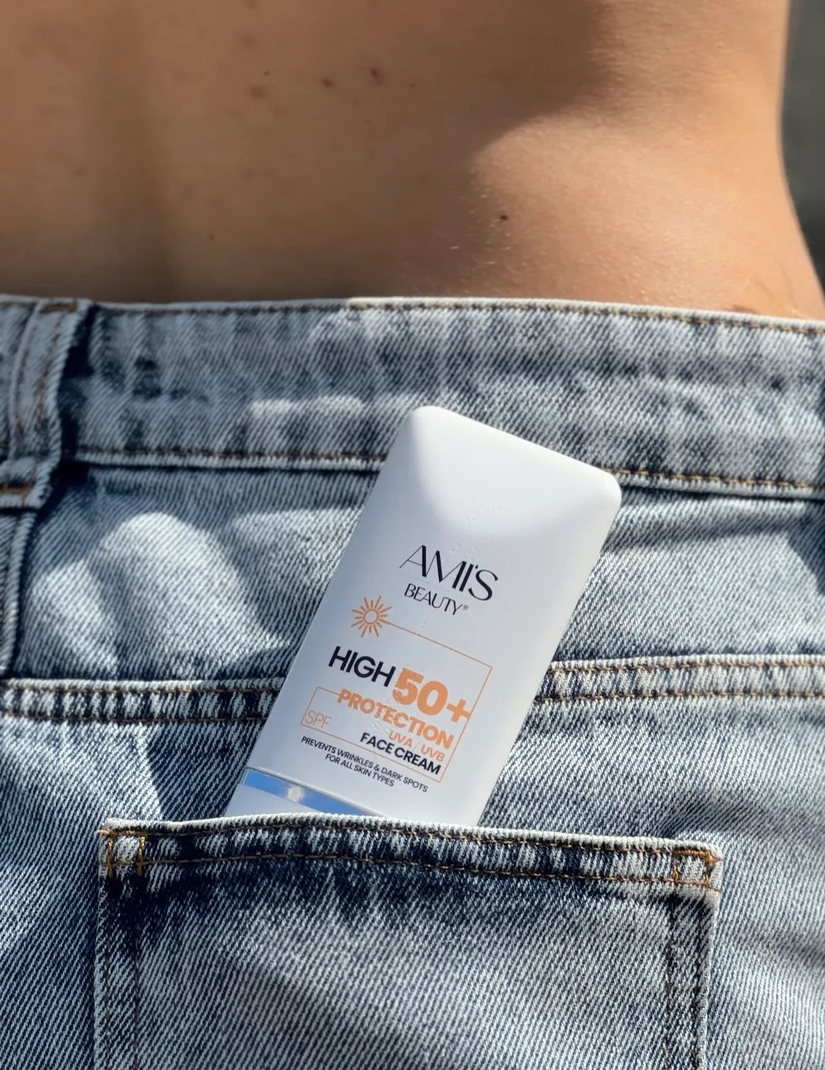 Tube of Krem dielli SPF 50+ tucked into the back pocket of light blue denim jeans.