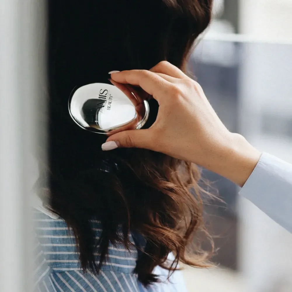 Person brushing their long, dark wavy hair with a silver mini hairbrush.