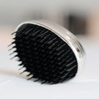 Close-up showing the black bristles of a round, metallic mini hairbrush resting on a light surface.