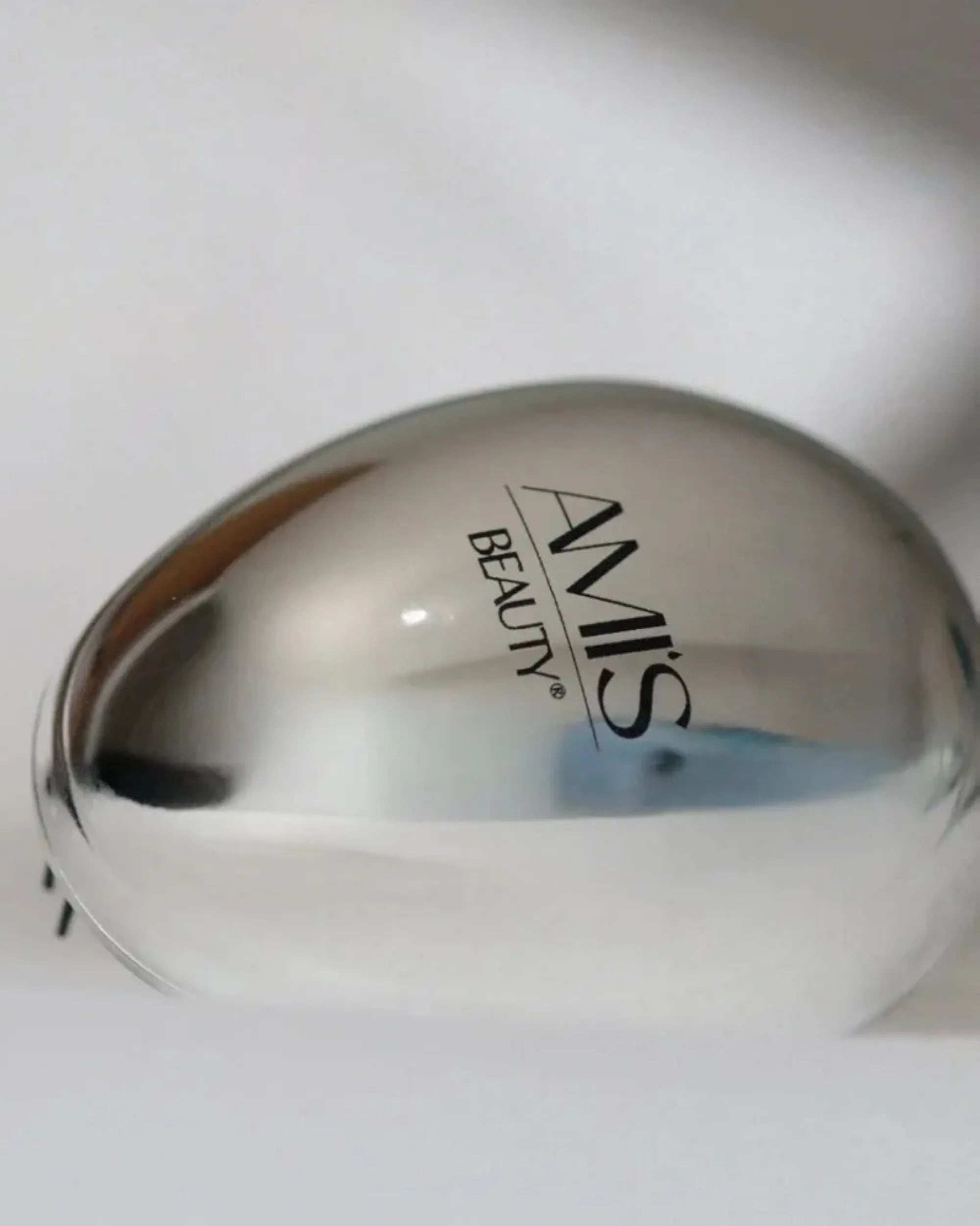 Smooth, reflective silver back of a round mini hairbrush.