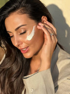 Smiling woman outdoors in the sunlight applying a streak of Krem dielli SPF 50+ to her cheek.