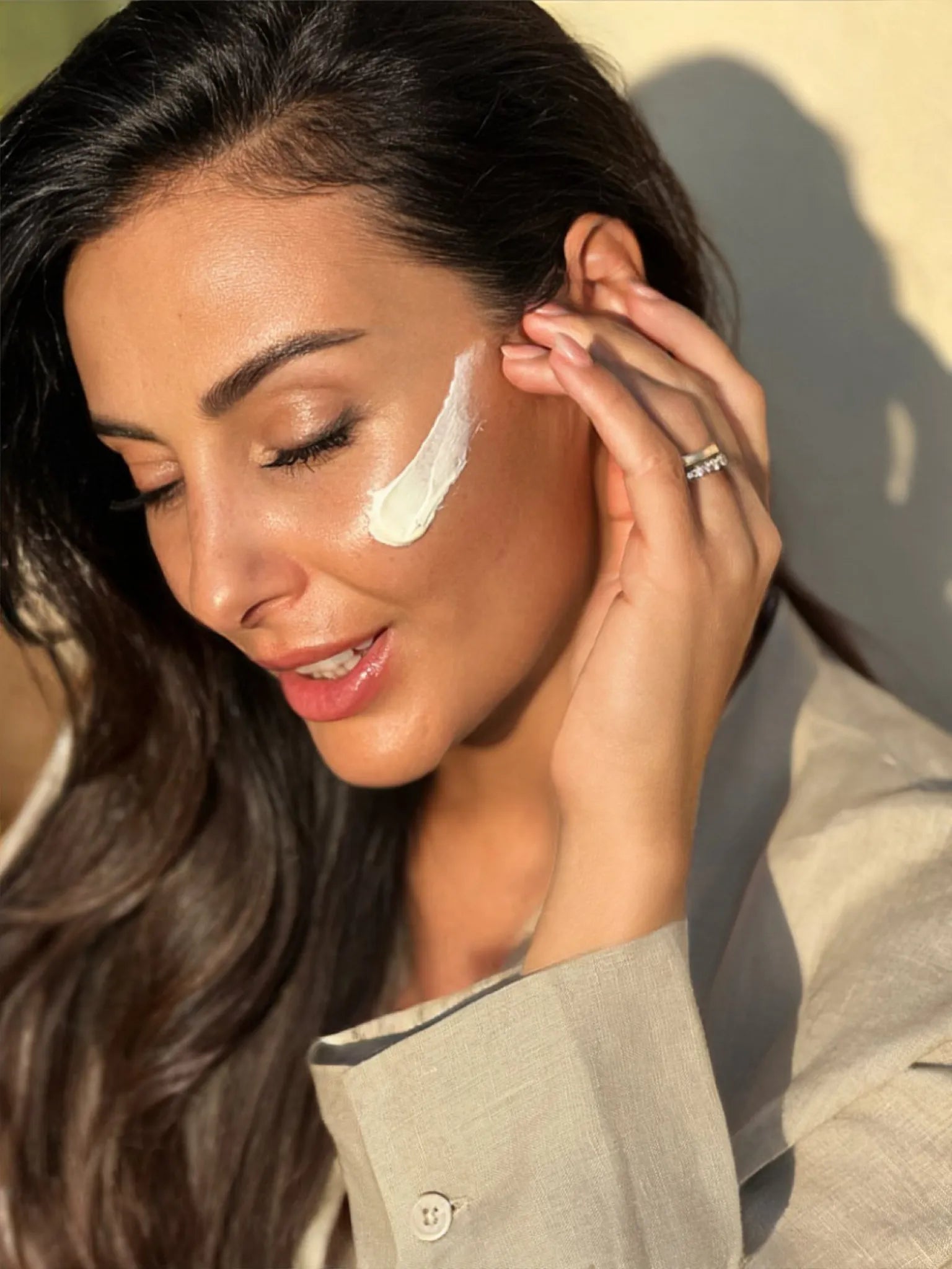 Smiling woman outdoors in the sunlight applying a streak of Krem dielli SPF 50+ to her cheek.