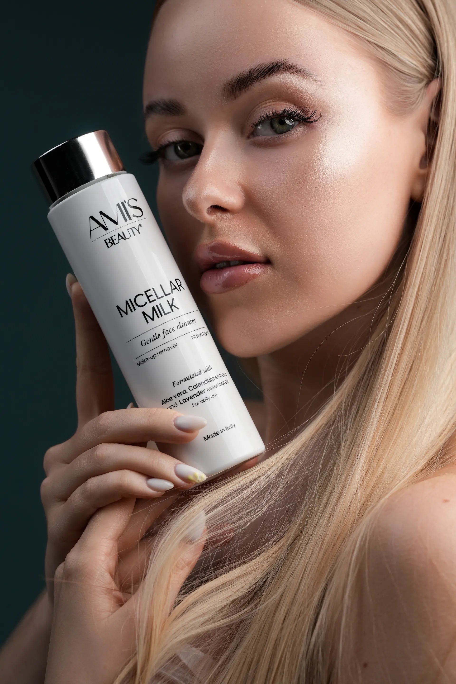 Woman with long blonde hair holding a white bottle of Micellar Milk up to her face against a dark background.