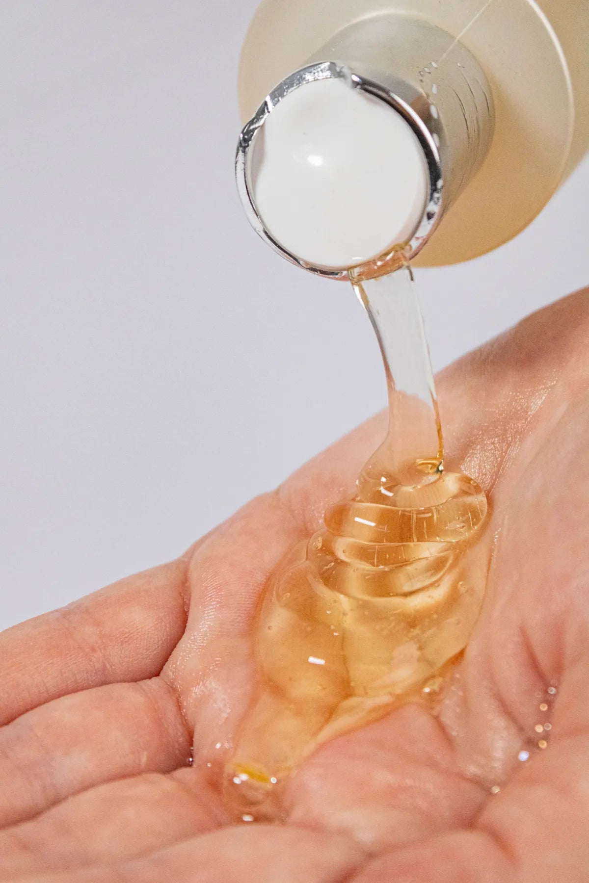 Close-up of golden Curly Crush Conditioner being poured into a person's hand.