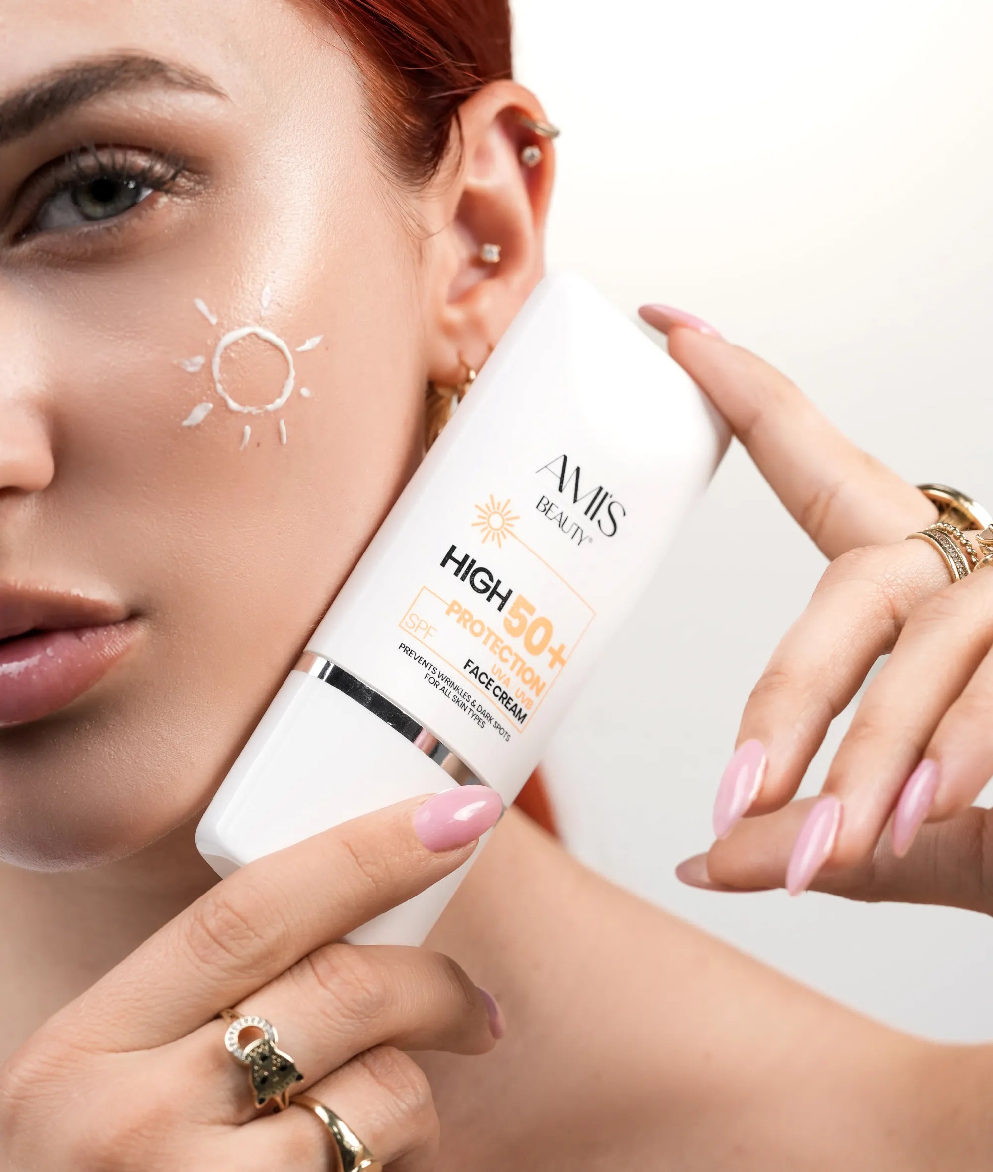 Close-up of a woman holding a tube of Krem dielli SPF 50+ next to her face, with a streak of the product on her cheek.